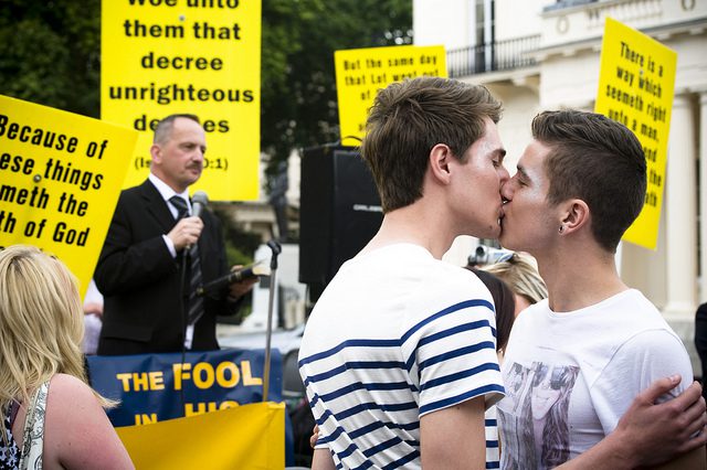 Two young men kissing in front of a crowd of people.