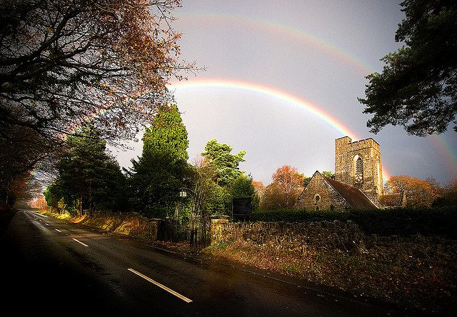 Bright twin rainbows over stone church by road