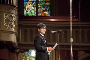 A man in a tuxedo standing in front of a stained glass window.