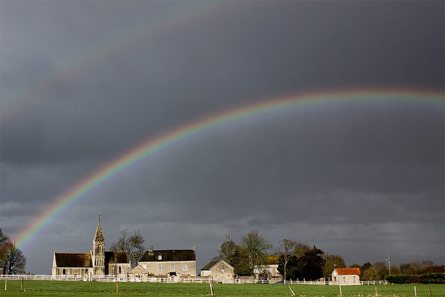 A rainbow over a church in a field.