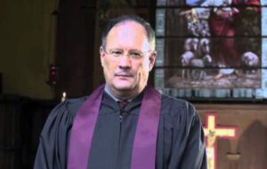 A man in a black robe standing in front of a church.