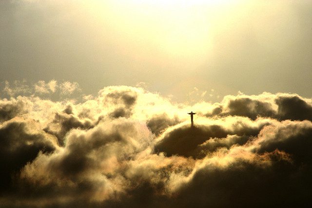 A cross in the clouds with the sun shining behind it.