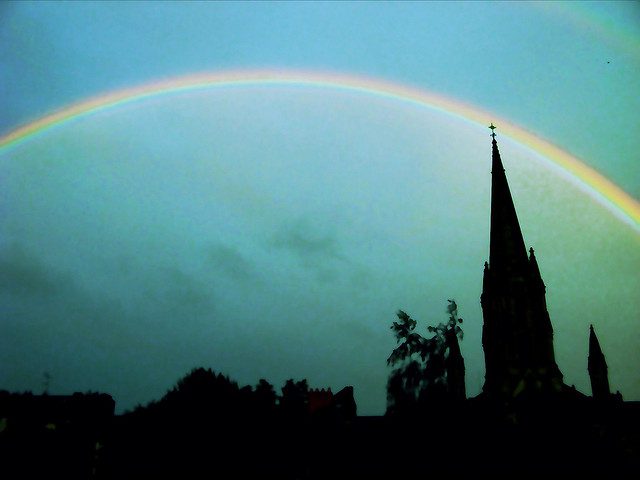 Vibrant rainbow arch above silhouetted church steeple