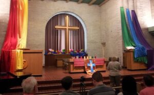 A group of people standing in front of a rainbow cross in a church.