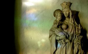 A statue of mary holding a child in front of a stained glass window.