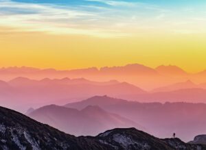 A person is standing on top of a mountain at sunset.