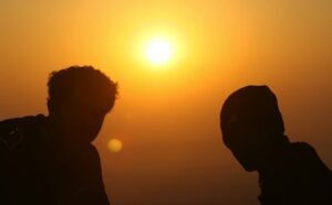Two men standing on top of a mountain at sunset.