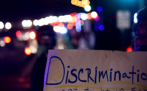 A woman holds up a sign that says discrimination is not ok.