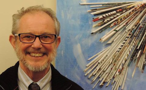 A man smiling in front of a wall of paper.