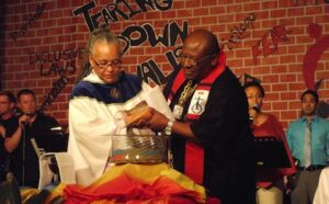 A man is pouring a cup of water on a man in front of a crowd.