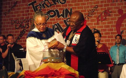 A man is pouring a cup of water on a man in front of a crowd.