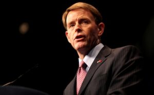 A man in a suit and tie speaking into a microphone.