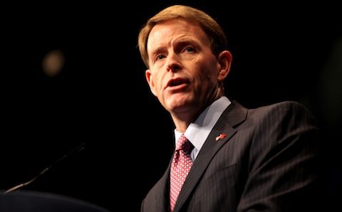 A man in a suit and tie speaking into a microphone.
