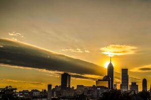 The sun is setting over a city with a cloud in the sky.