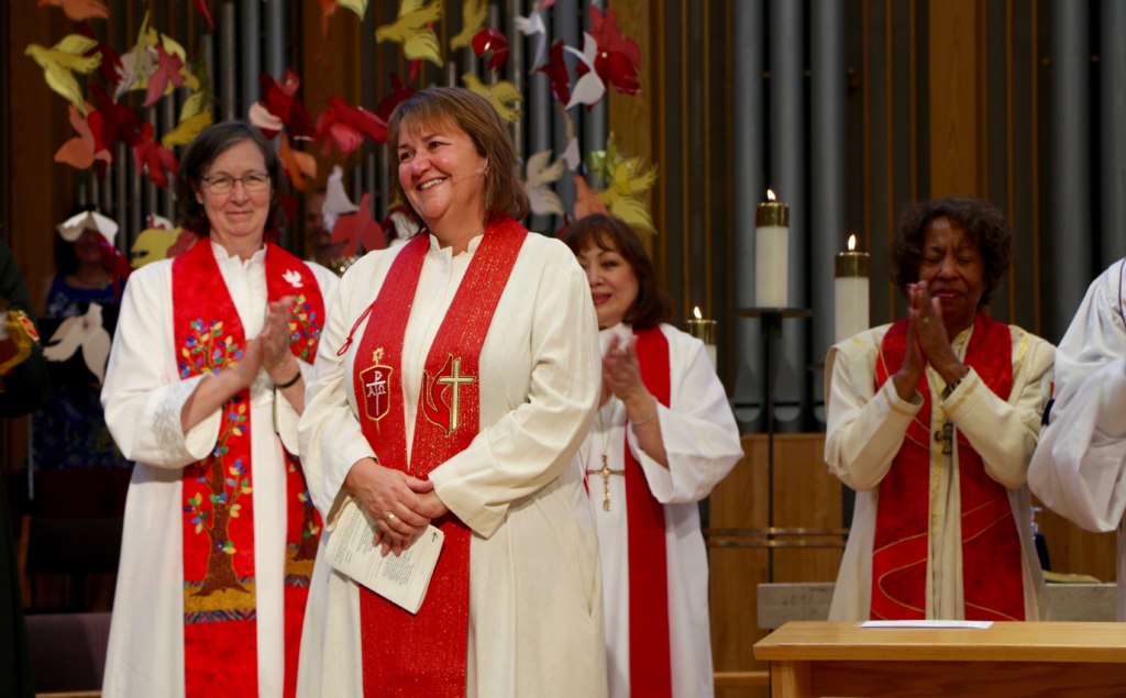 Clergywomen in robes clapping during ceremony.