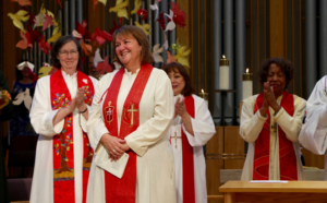 Clergywomen in robes clapping during ceremony.