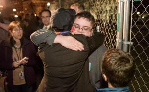 People hugging near a chain-link fence.