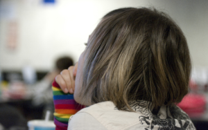 Person with rainbow sleeve, short hair, thoughtful.
