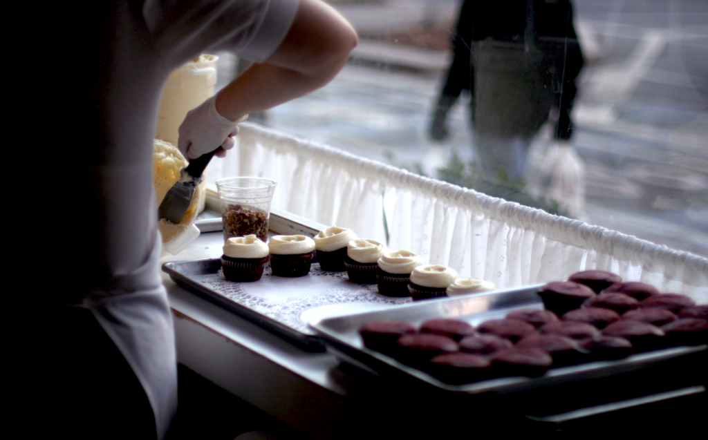 Person decorating cupcakes in a bakery window.