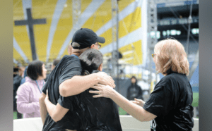 A group of people hugging in front of a cross.
