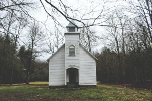 A small white church in the middle of a wooded area.