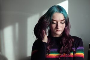 A woman with rainbow hair sitting in front of a window.